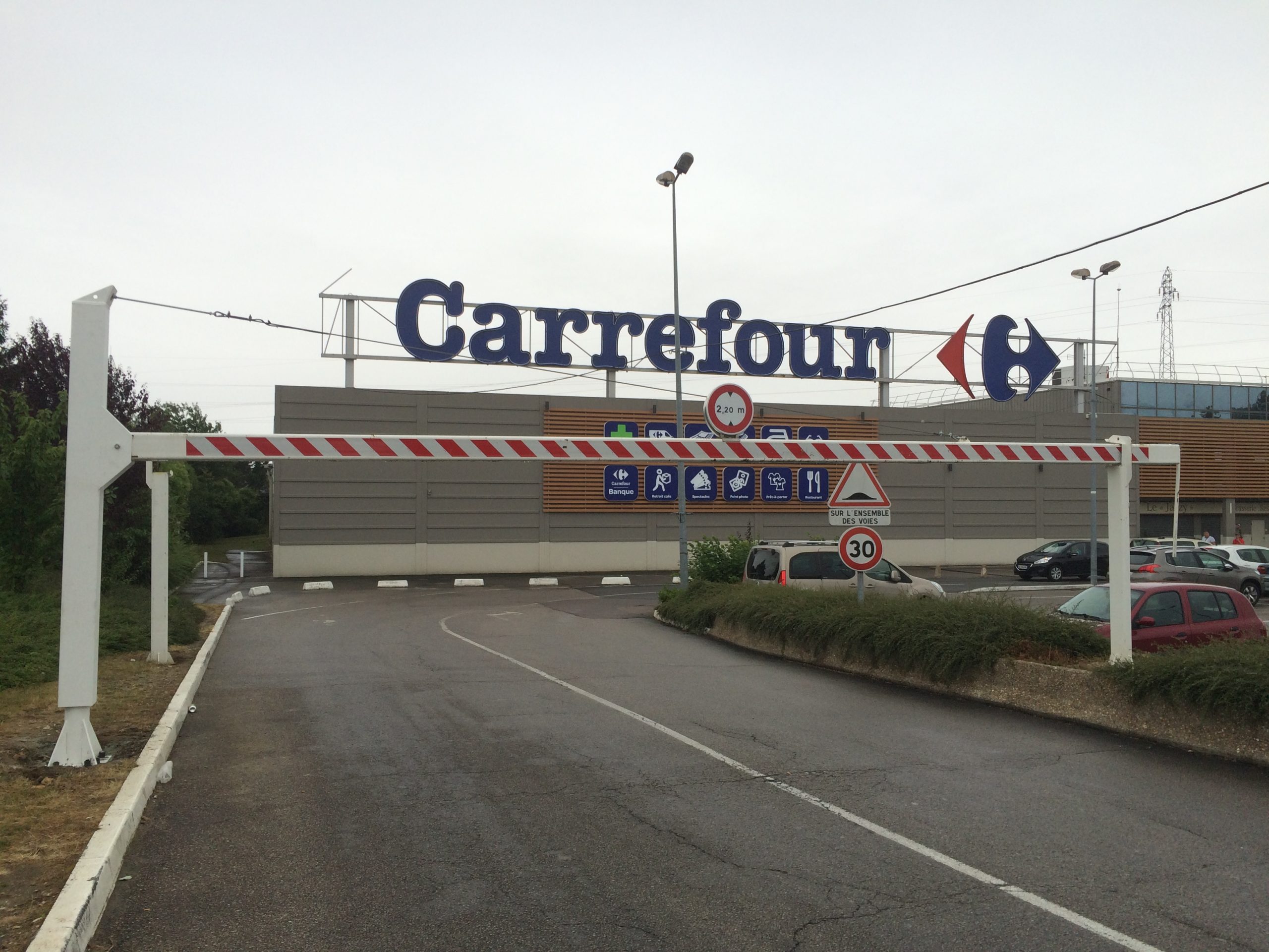 Poutre pivotante manuelle rouge en position ouverte sur un parking Carrefour
