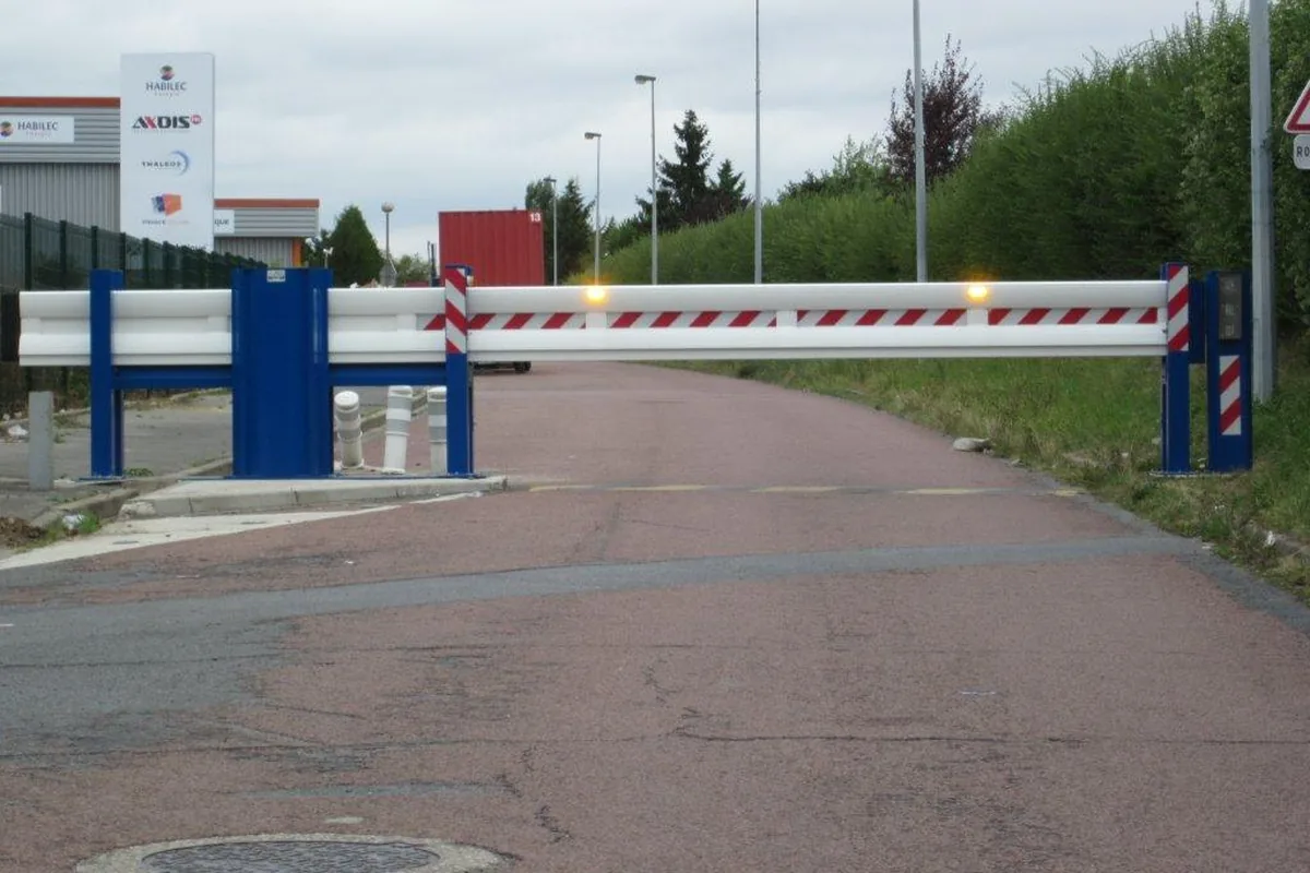 Poutre coulissante motorisée bleue et blanche fermant l'accès d'une zone d'activité, avec glissière de sécurité et feux orange, JCD Services