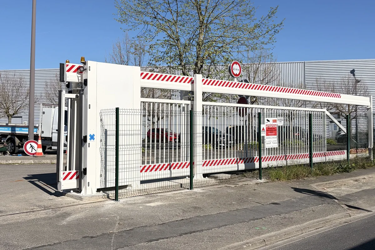 Poutre coulissante motorisée blanche avec limitation de hauteur à 2,10 m fermant l'accès d'un site industriel, installée par JCD Services