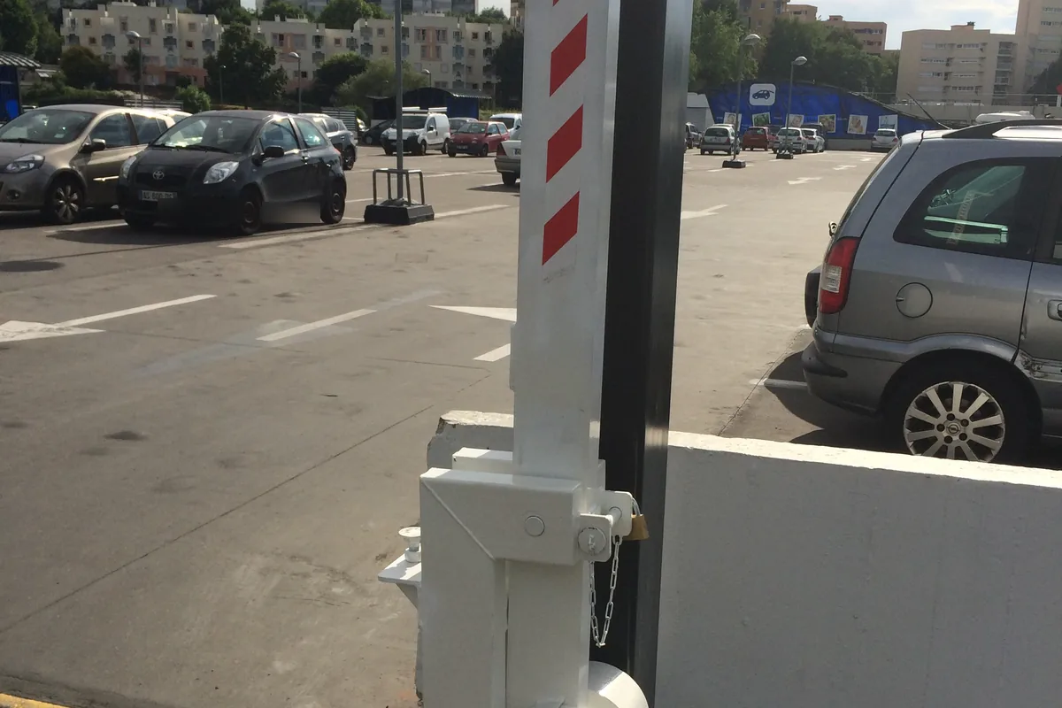 Barrière levante manuelle et son verrouillage par cadenas sur un parking, JCD Services